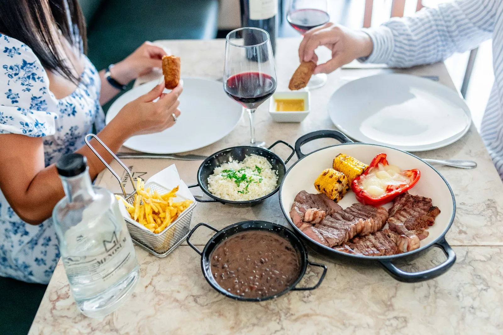 Almoço no MENOSUM com carne, arroz, feijão, batatas e vinho à mesa